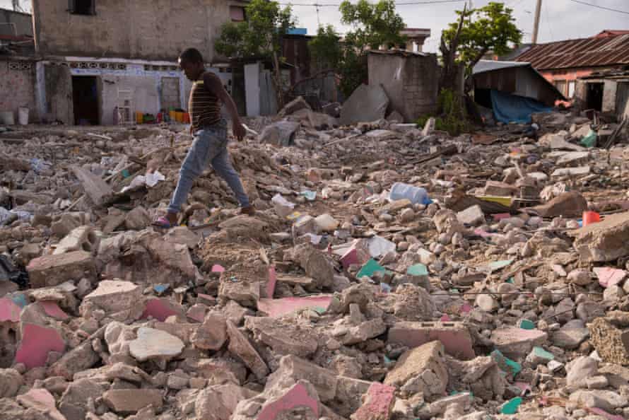 A boy walks over the rubble of a house.