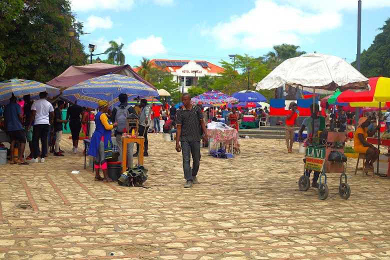 A man walks past food carts under umbrellas at Place d’Armes in Cap-Haïtien during Agriculture Day on May 1, 2025. Photo by Onz Chéry / The Haitian Times.