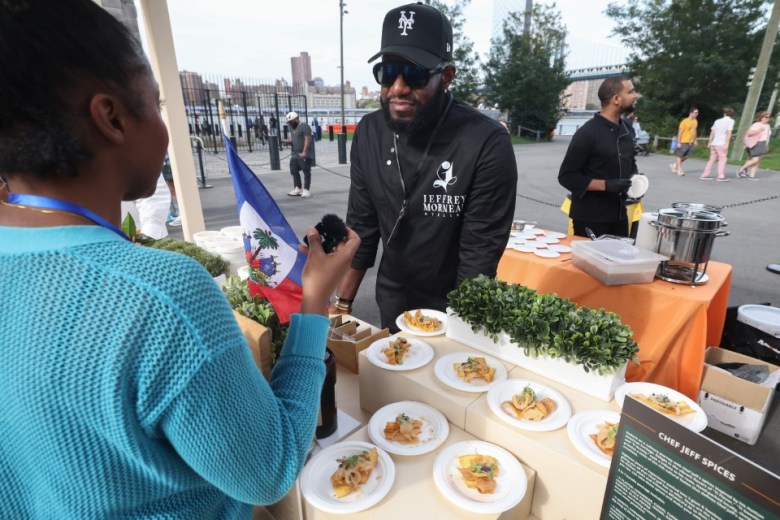 Chef Jeffrey Morneau speaks with a guest at the Creole Food Festival in Brooklyn on Saturday, Sept. 27, 2025. The festival ran Sept. 26–28 at Emily Roebling Plaza under the Brooklyn Bridge. Morneau and his team served lambi pike (conch salad) and soup joumou. Photo by Bill Farrington.
