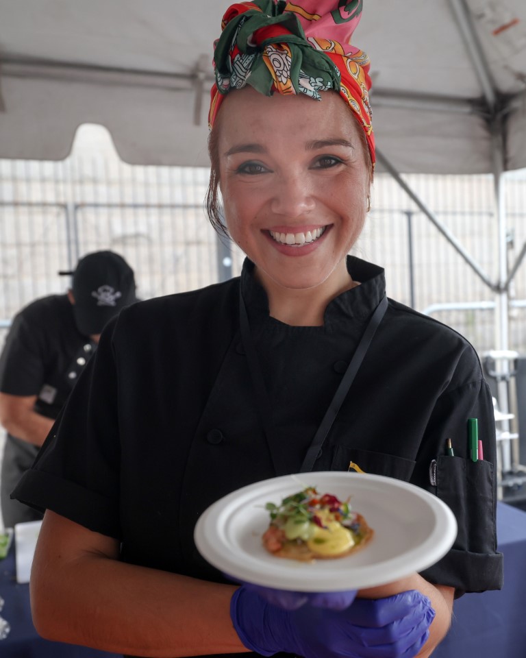 Chef Vanessa Ceballos of Venezuela prepares arepa crackers with shrimp and octopus carpaccio and guasacaca, a green sauce made with herbs and avocado, dressed with a passion fruit vinaigrette. The dish sold out quickly at the Creole Food Festival in Brooklyn on Saturday, Sept. 27, 2025, at Emily Roebling Plaza under the Brooklyn Bridge. Photo by Bill Farrington.
