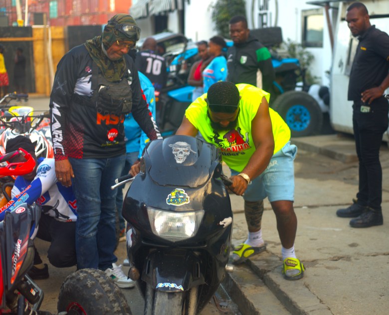 A man pushes a motorcycle along the roadside before the start of the Ruff Ryders Block Party on March 7, 2026, in Cap-Haïtien. Photo by Onz Chéry / The Haitian Times.
