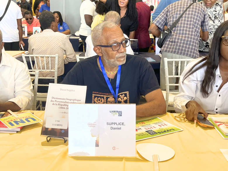Haitian writer Daniel Supplice sits at a table at the 32nd edition of Livres en Folie at the El Rancho Hotel in Pétion-Ville on Thursday, June 4, 2026. Photo by Juhakenson Blaise / The Haitian Times