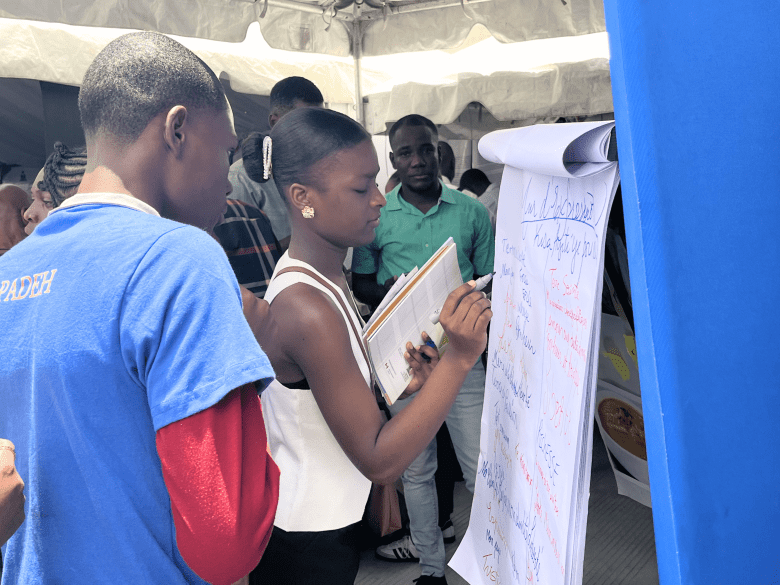 Children at the UNESCO pavilion write about what Haiti represents to them during the 32nd edition of Livres en Folie at the El Rancho Hotel in Pétion-Ville on Thursday, June 4, 2026. Photo by Juhakenson Blaise / The Haitian Times