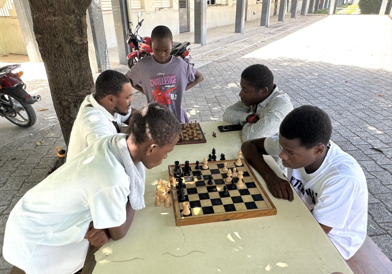 Two young men and children play chess during “Let’s Play Together” on Saturday, Aug. 15, 2026, at Lycée Anacaona in Léogâne, Haiti. Photo by Daniella Saint-Louis for The Haitian Times.